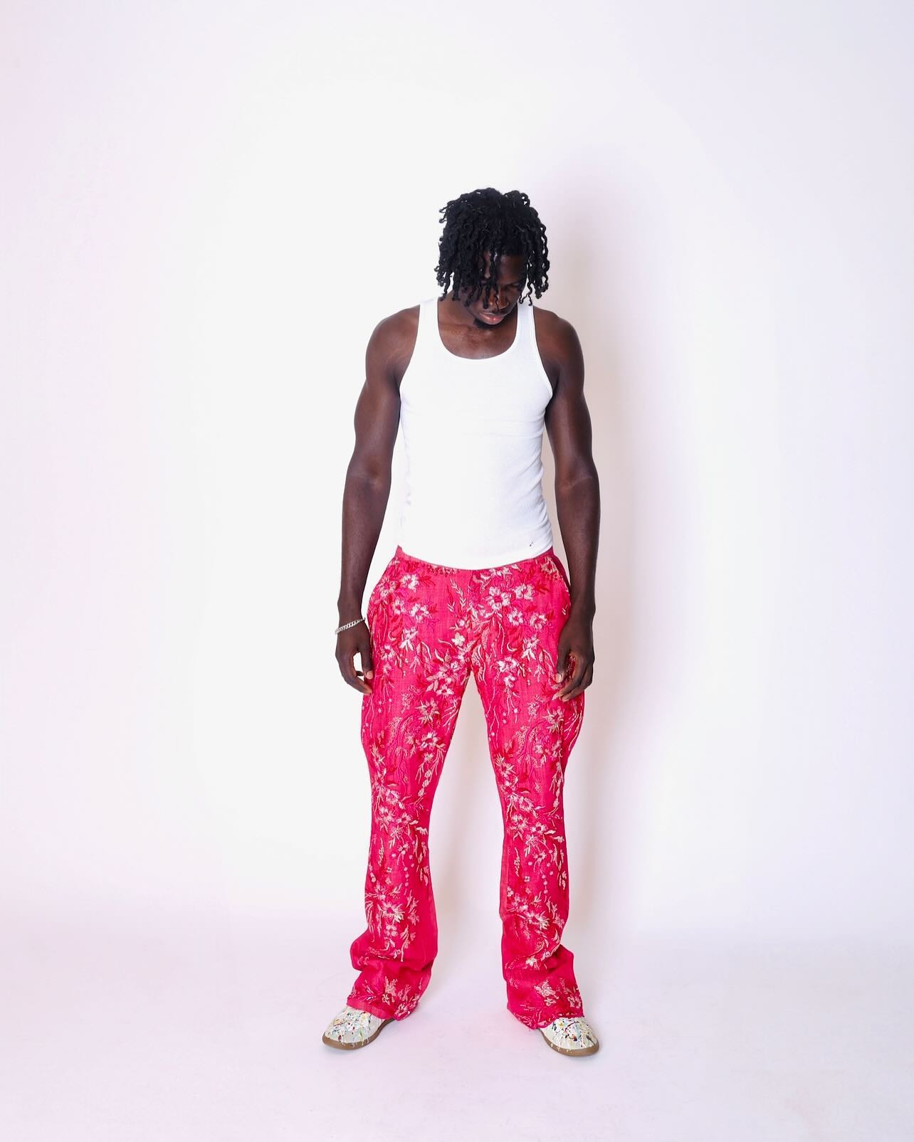 Person wearing a white tank top and pink floral pants on a white background