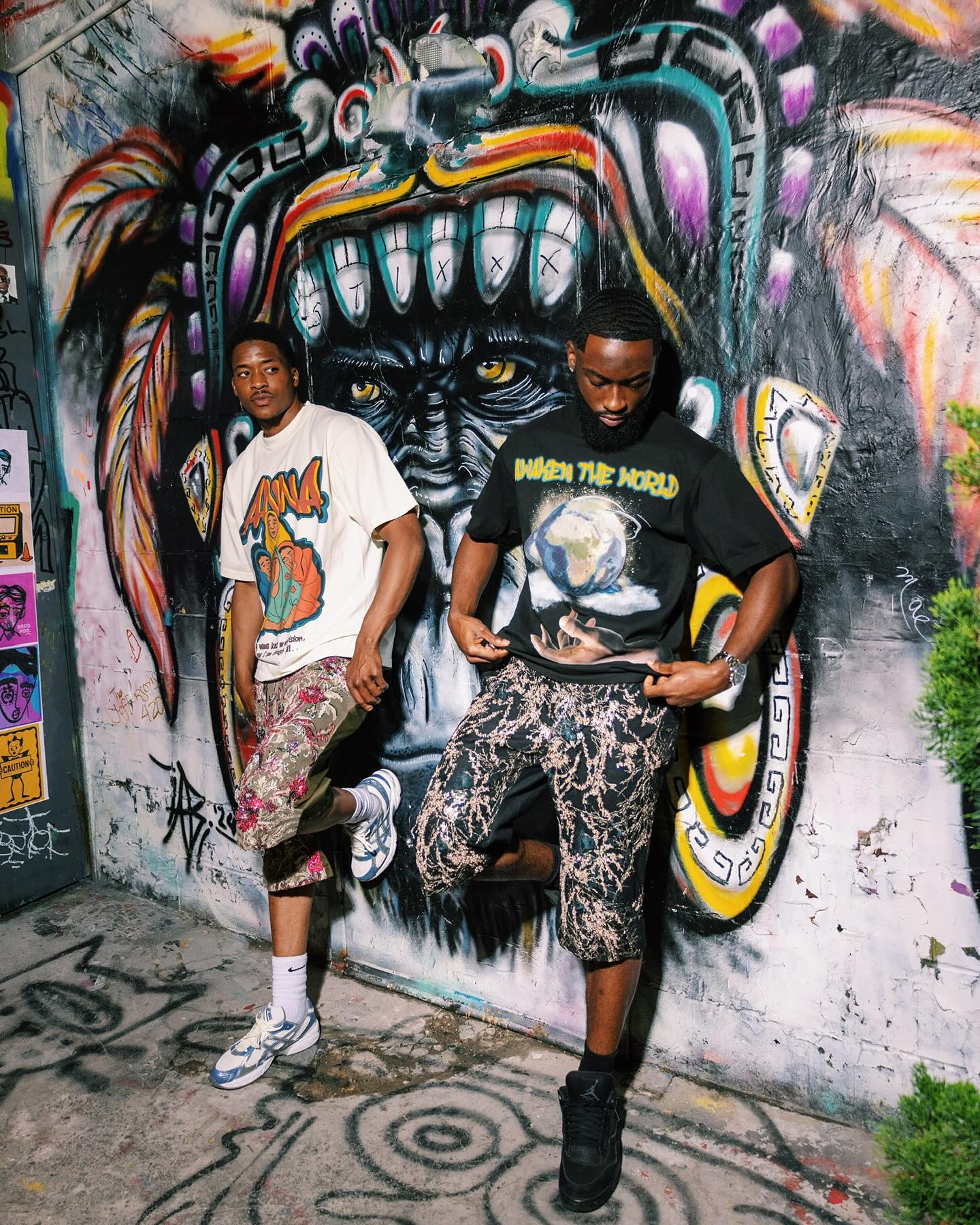 Two people standing in front of a colorful mural with graffiti on the wall.