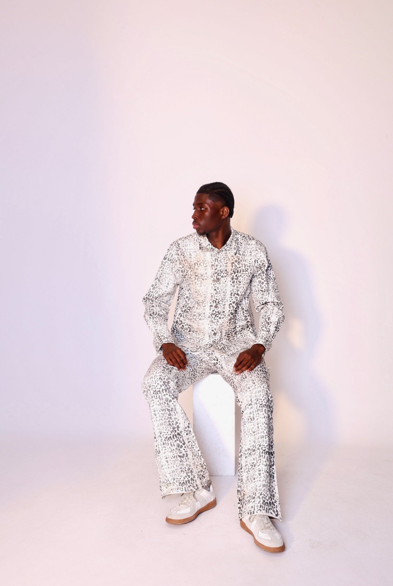 Person wearing a white patterned outfit sitting against a light background