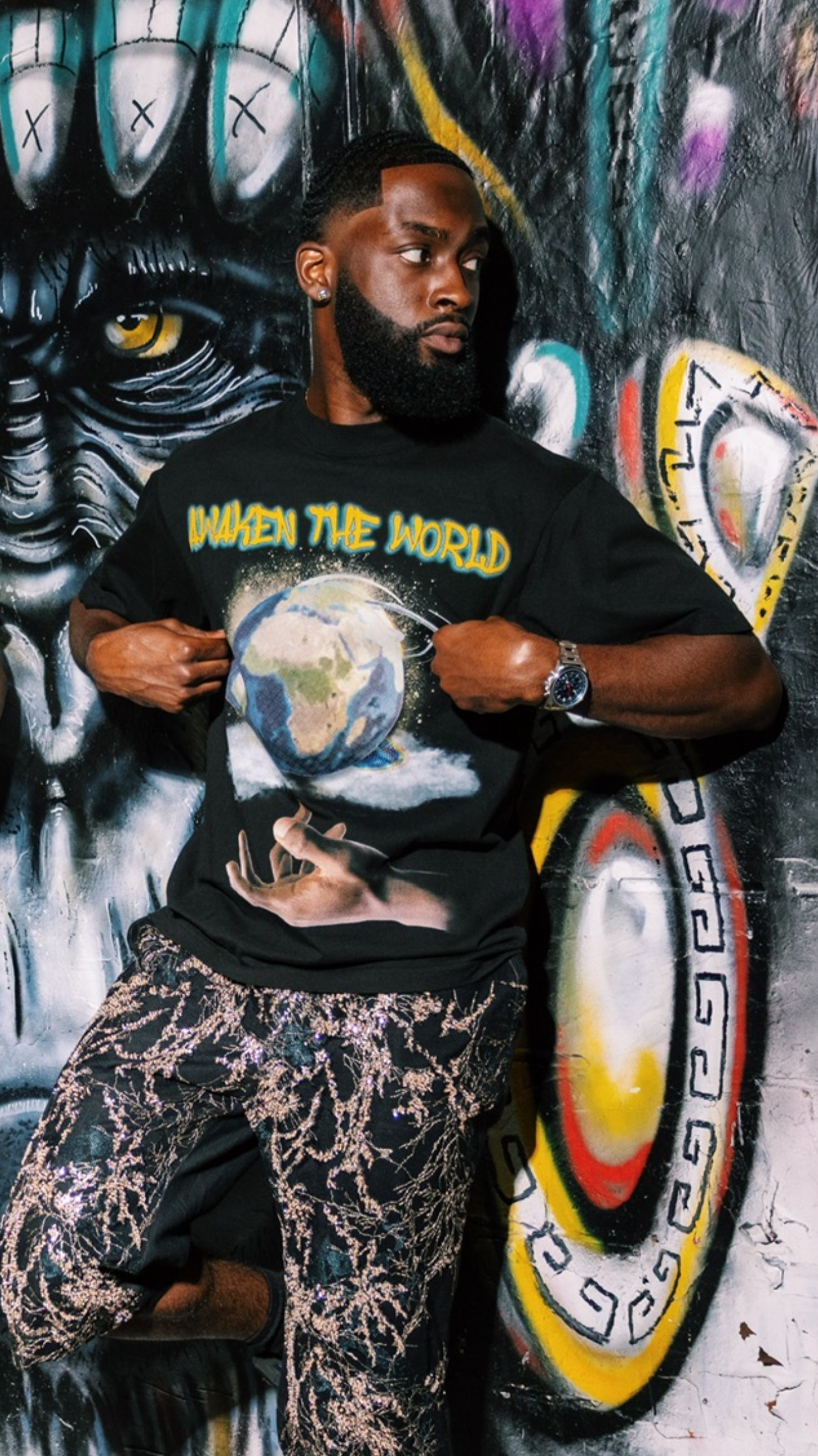 Person wearing a black t-shirt with a graphic design and text, standing in front of a colorful mural.